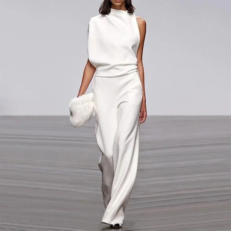 Model wearing a white asymmetric sleeveless gown and holding a white fur clutch on runway