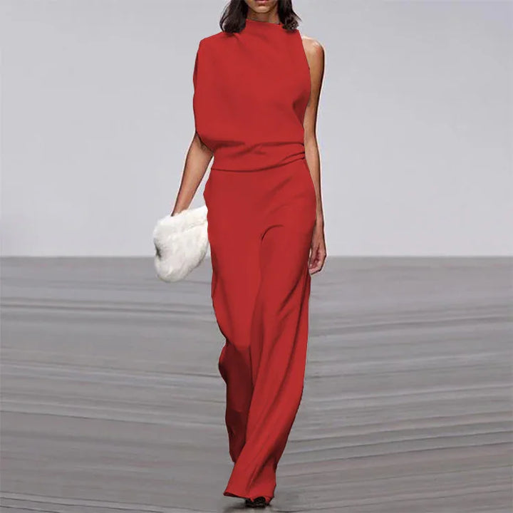 Model walking runway in elegant red sleeveless jumpsuit holding white fur clutch bag