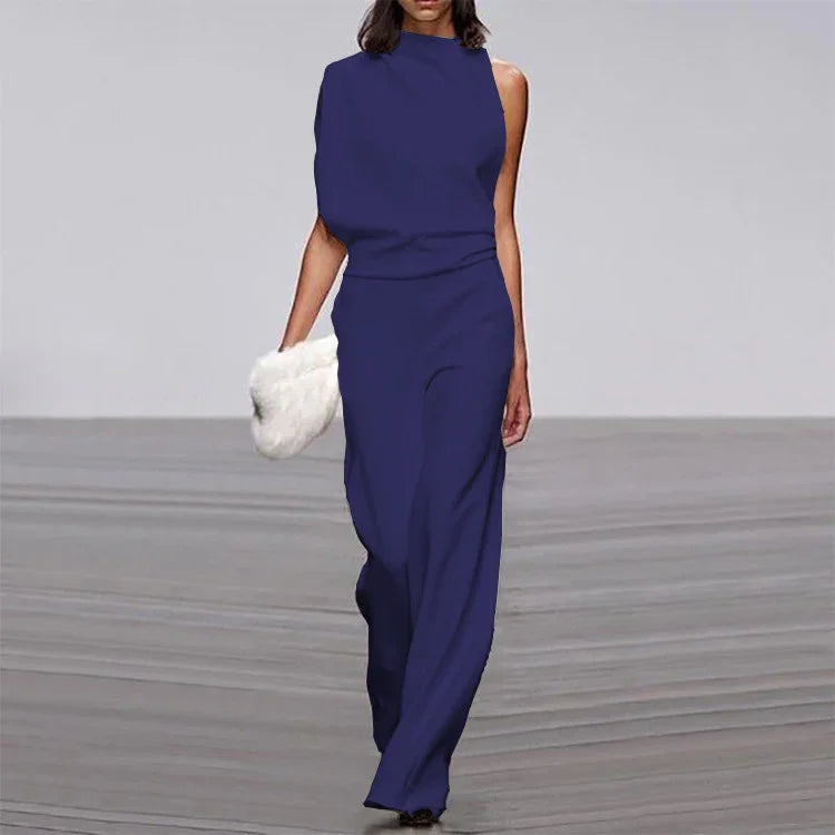 Model wearing a navy blue sleeveless asymmetrical jumpsuit holding a white fur clutch on runway