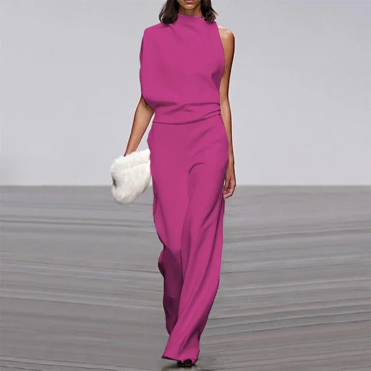 Model wearing a sleek magenta sleeveless jumpsuit walking on runway holding a white fur clutch