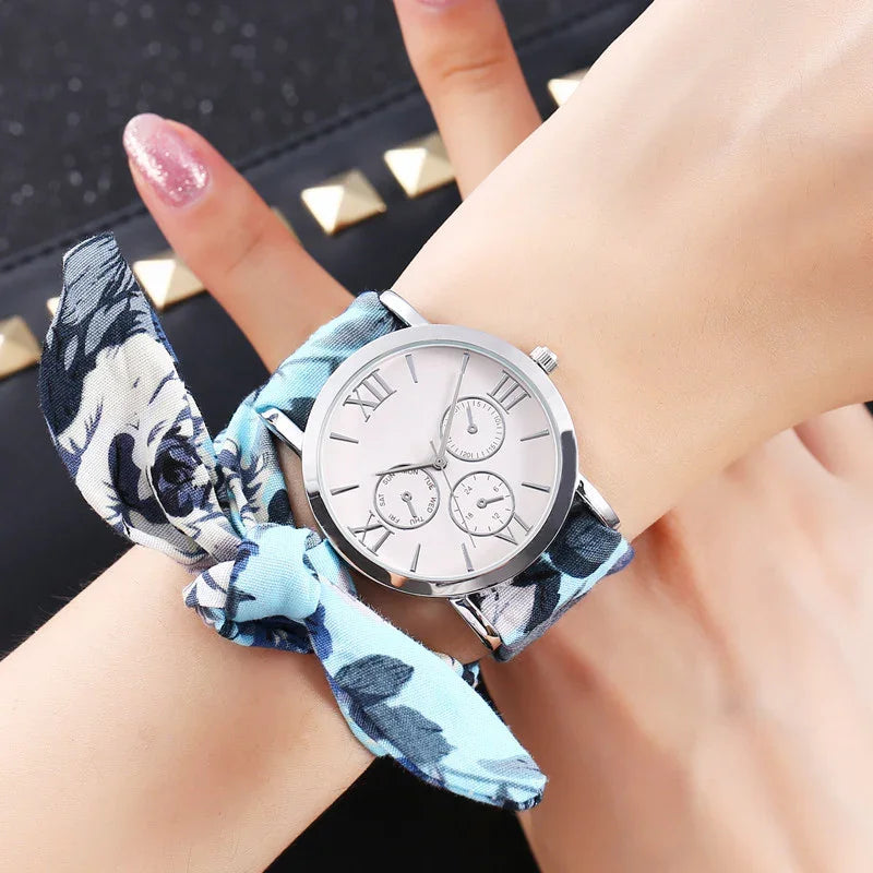 Silver round watch with white dial and Roman numerals on wrist with blue floral fabric band
