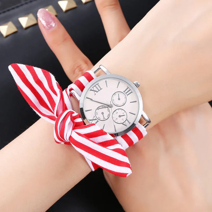 Woman's wristwatch with a white dial, roman numerals, and red and white striped fabric strap tied in a bow