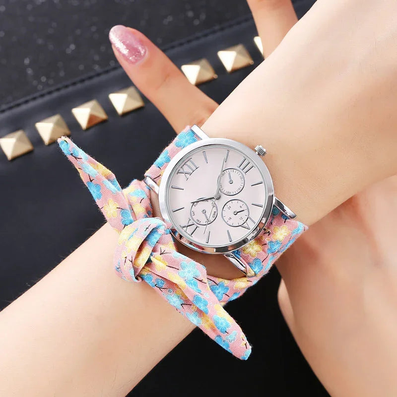 Silver wristwatch with Roman numerals and floral fabric strap tied in a bow on wrist