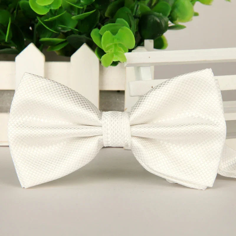 Elegant white textured satin bow tie on a white surface with green plants background