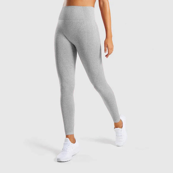 Woman wearing high-waisted light grey textured leggings and white athletic shoes on gray background