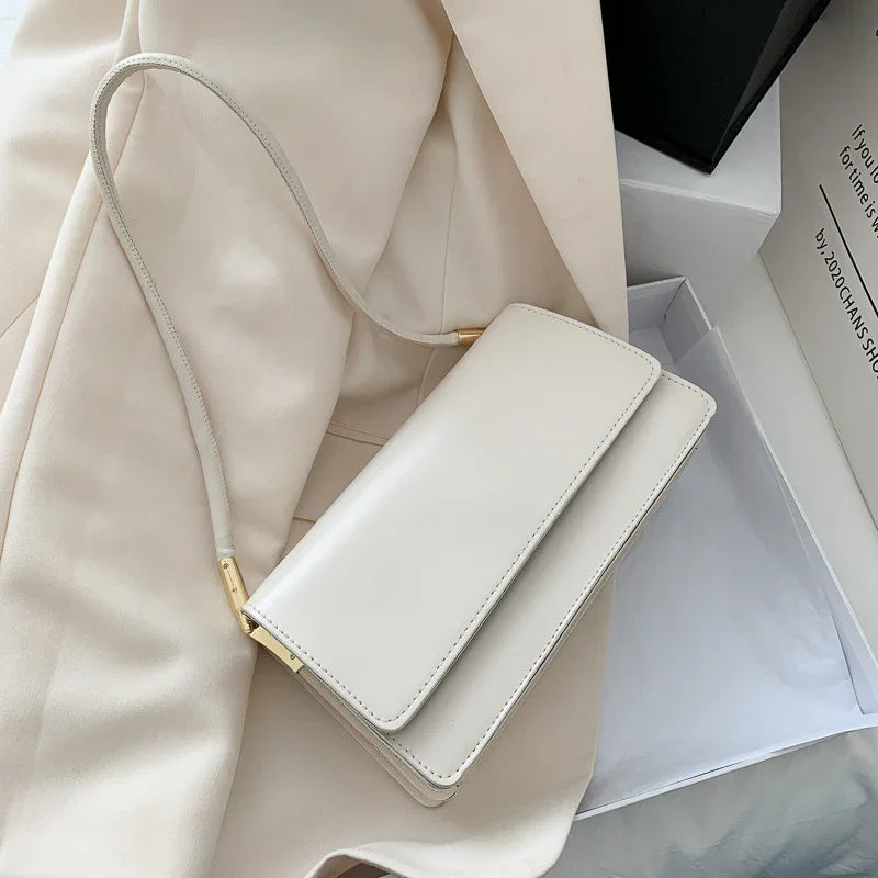Elegant white leather shoulder bag with gold accents on beige fabric next to open black and white boxes