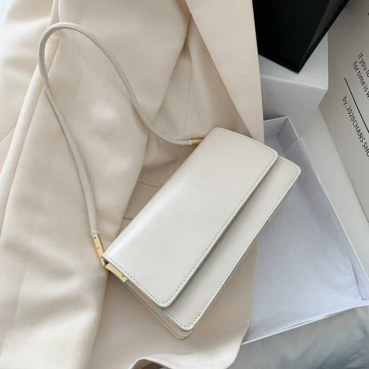 Elegant white leather shoulder bag with gold accents on beige fabric next to open black and white boxes
