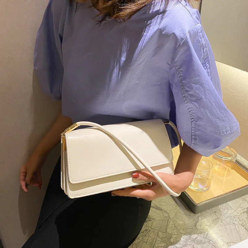 Woman in light purple blouse holding a white leather shoulder bag with gold accents indoors