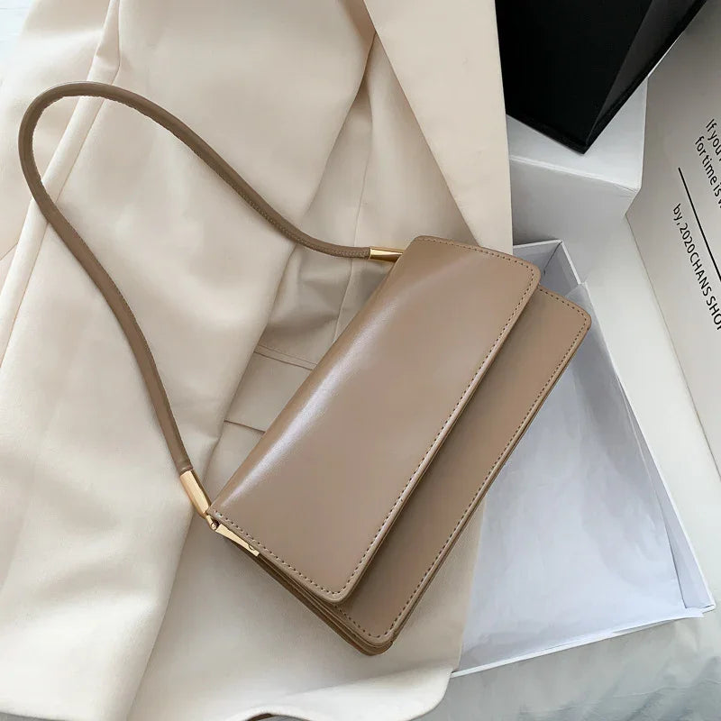 Beige leather handbag with a single strap on cream blazer near open white box