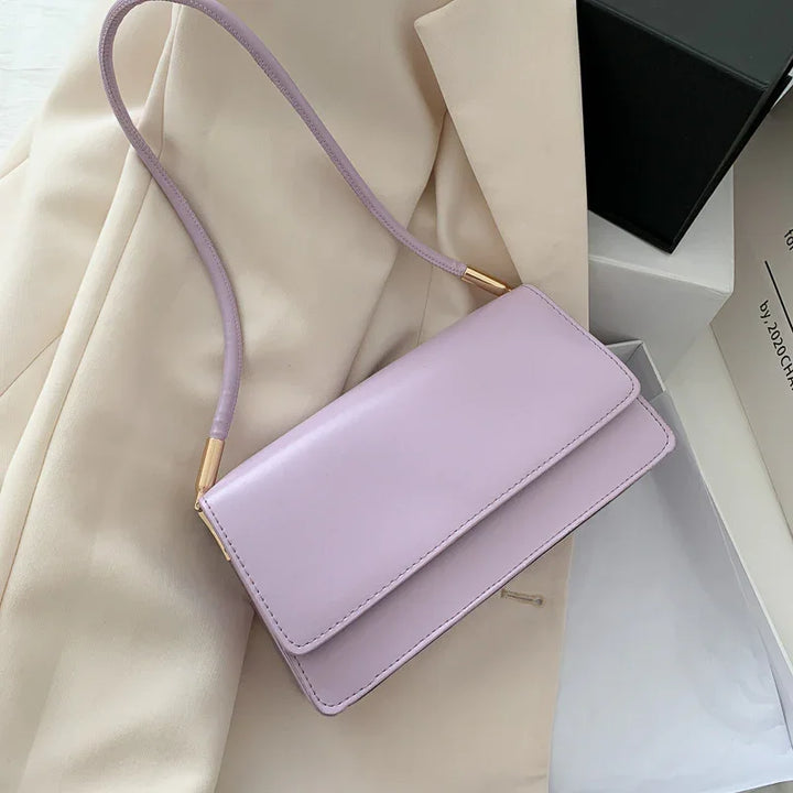 Lilac leather shoulder bag with gold accents on beige fabric background