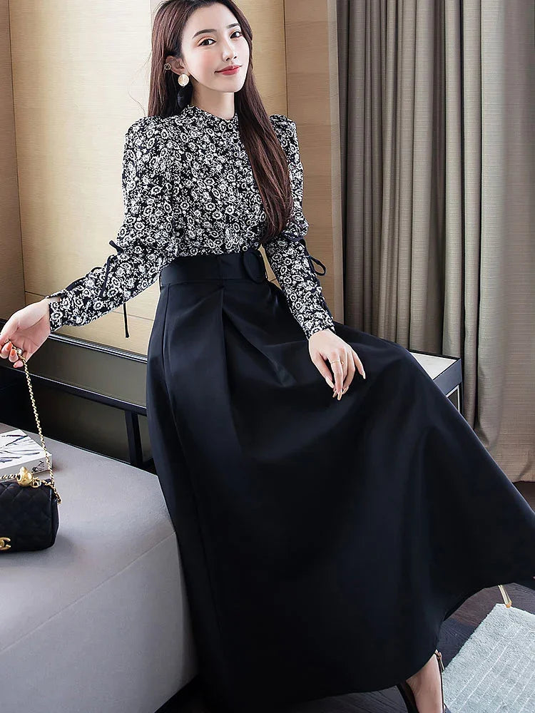 Woman wearing a black floral blouse with puff sleeves and a high-waisted black midi skirt, seated indoors