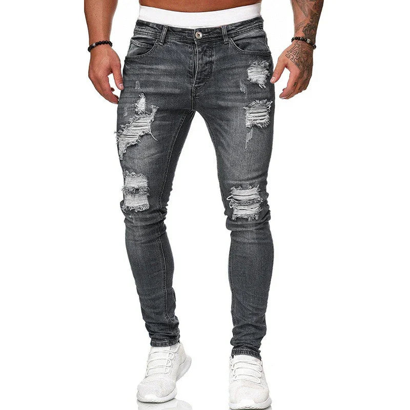 Men's slim fit black distressed ripped jeans paired with white sneakers and tattooed arms