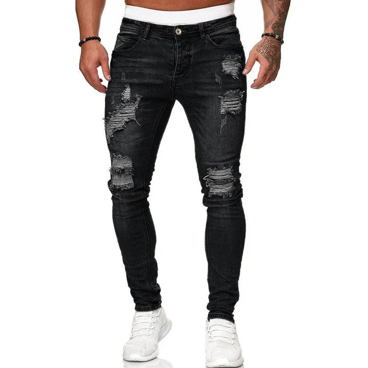 Man wearing black ripped skinny jeans and white sneakers with tattooed arms visible