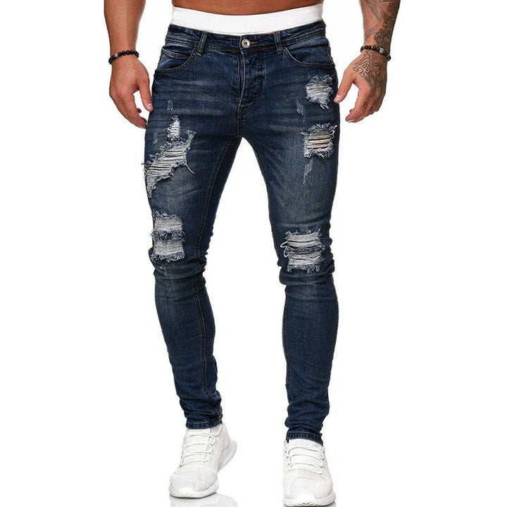 Mens dark blue ripped skinny jeans paired with white sneakers on a model against white background