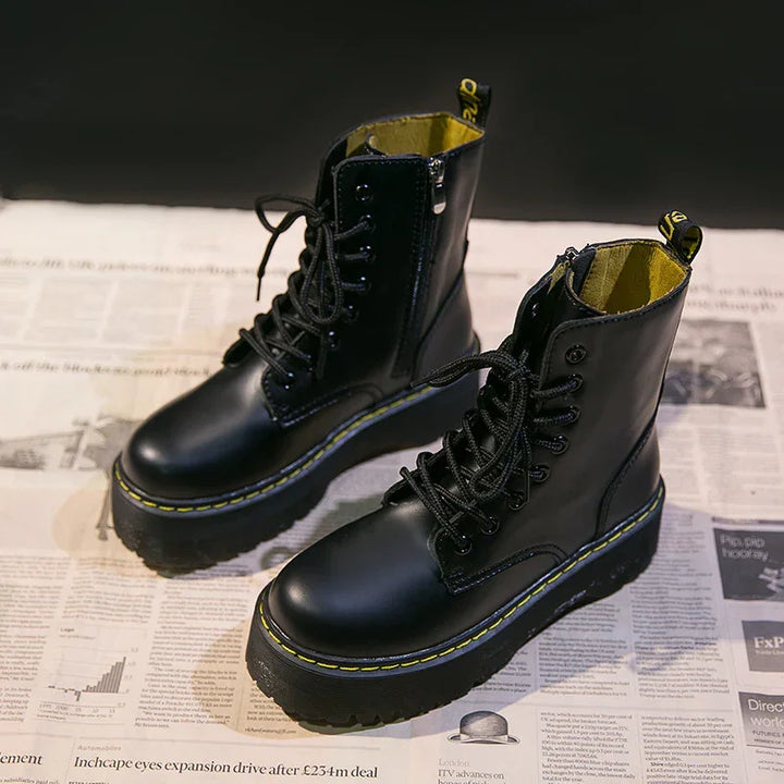 Black leather lace-up combat boots with yellow stitching on newspaper background