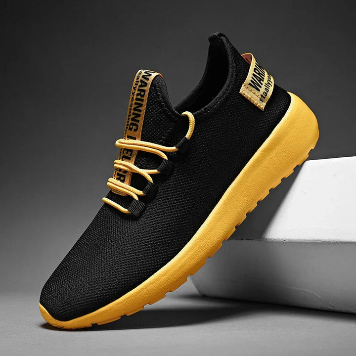 Black mesh sneaker with bright yellow sole and matching laces, warning label details on tongue and heel