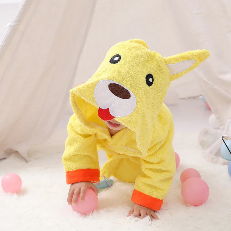 Baby crawling on white carpet in yellow dog-themed hooded towel with orange cuffs, surrounded by pink balls