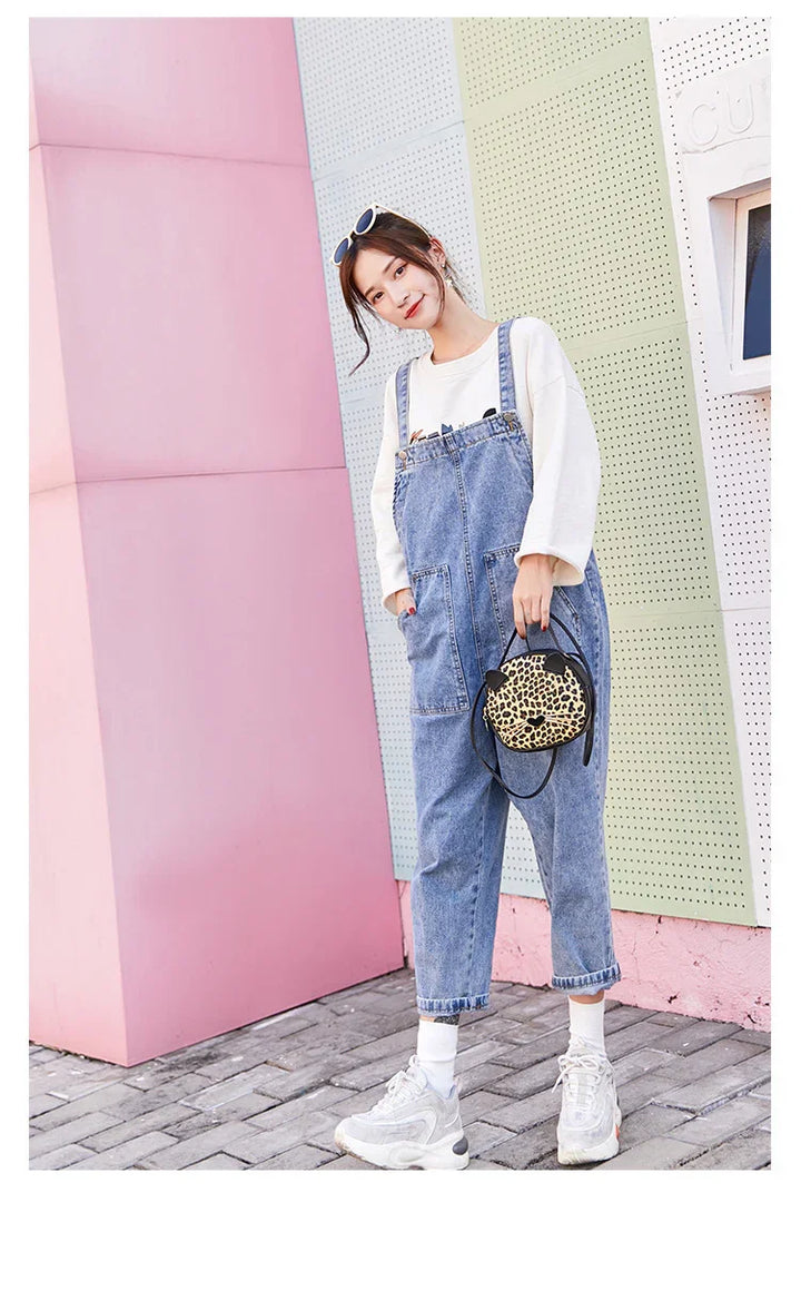 Young woman wearing denim overalls and white sweatshirt holding leopard print handbag against pastel wall