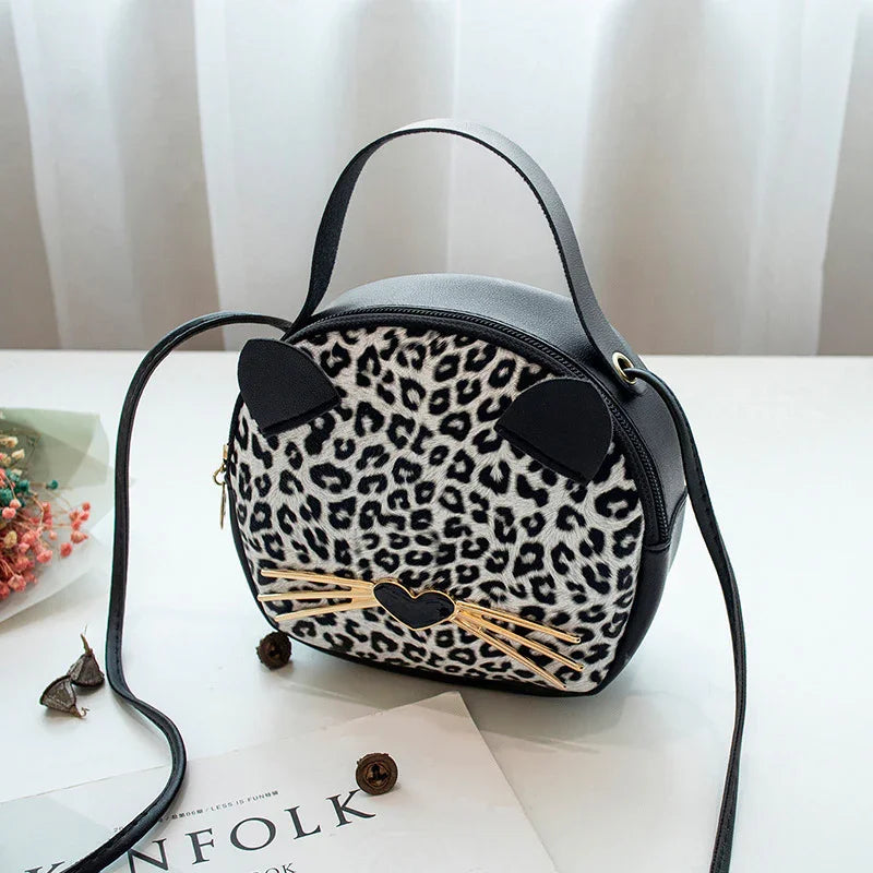 Small leopard print crossbody bag with cat ears and gold whiskers on white table