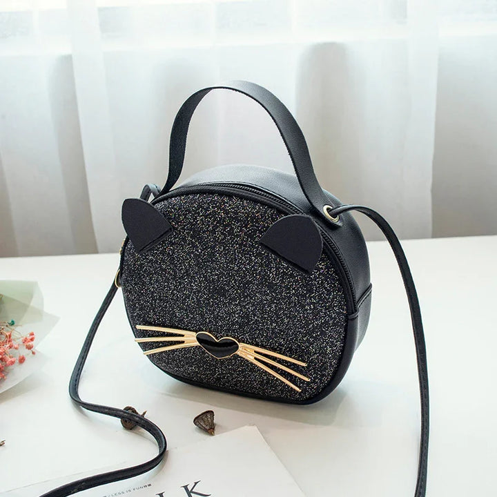 Black glitter cat face handbag with gold whiskers and heart-shaped nose on white table