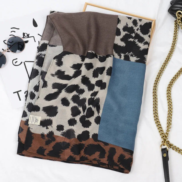 Folded leopard print scarf with brown, gray, and blue blocks, sunglasses, and gold chain purse on white