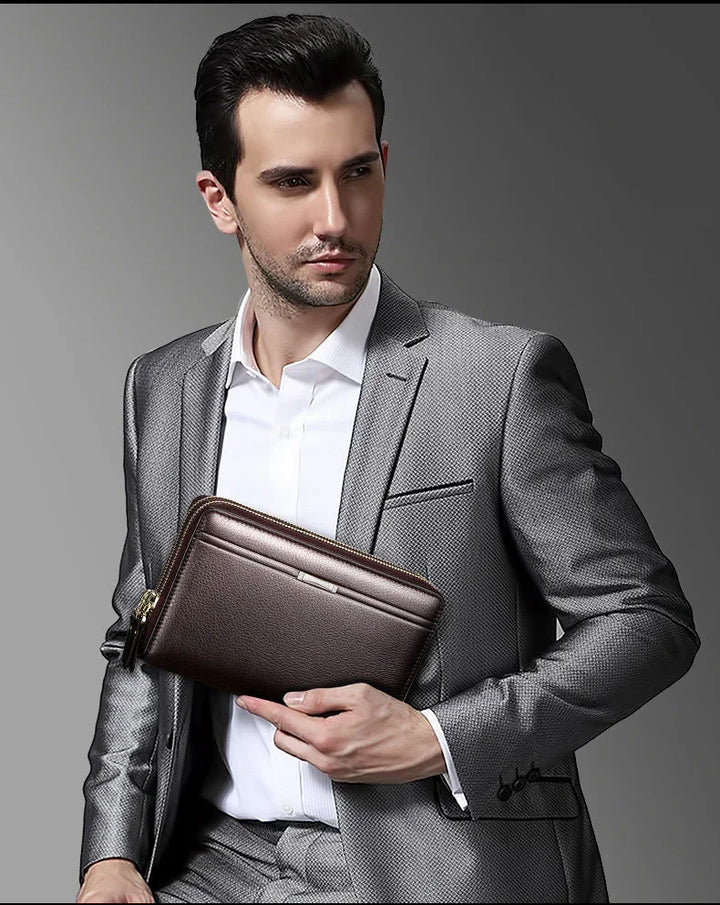 Man in silver suit holding dark brown leather zippered clutch bag against gray background