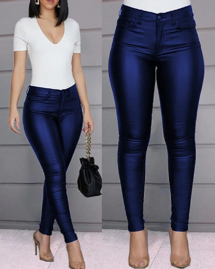 Woman wearing high-waisted shiny navy blue skinny jeans with a white V-neck top and clear heels
