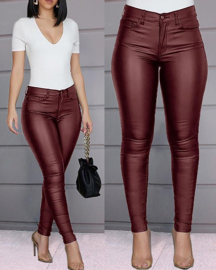 Woman modeling high-waisted burgundy faux leather skinny pants with a white fitted top and clear high heels