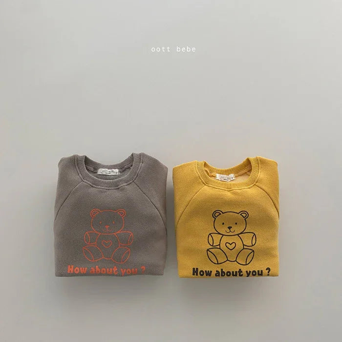 Folded baby sweatshirts in gray and mustard yellow with teddy bear print and text 'How about you?' on light background