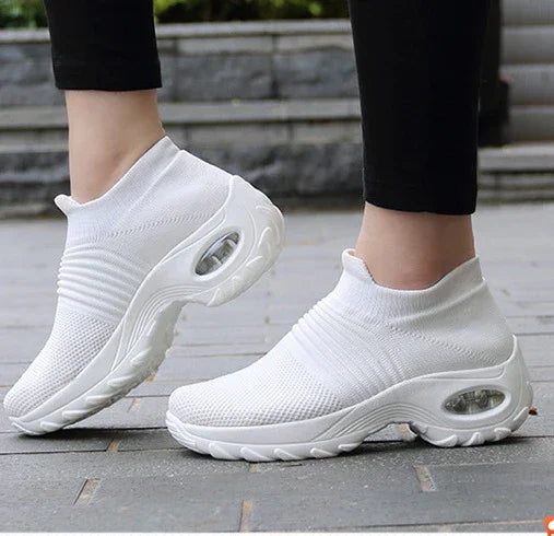 Pair of white slip-on sneaker shoes with air-cushioned soles worn with black leggings on pavement