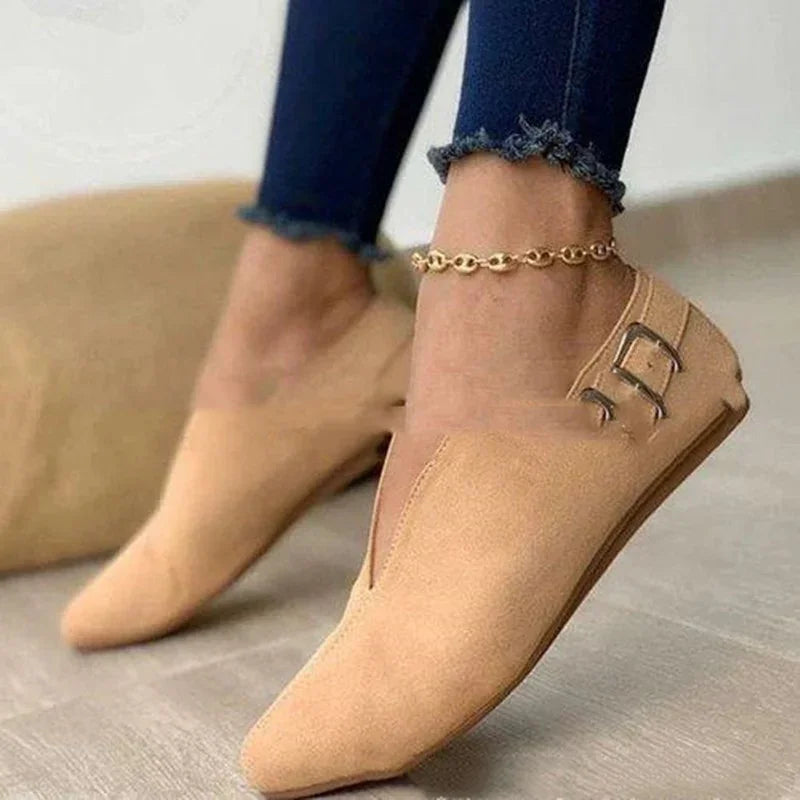 Beige flat shoes with buckles worn with dark blue frayed hem jeans and a gold anklet on wooden floor