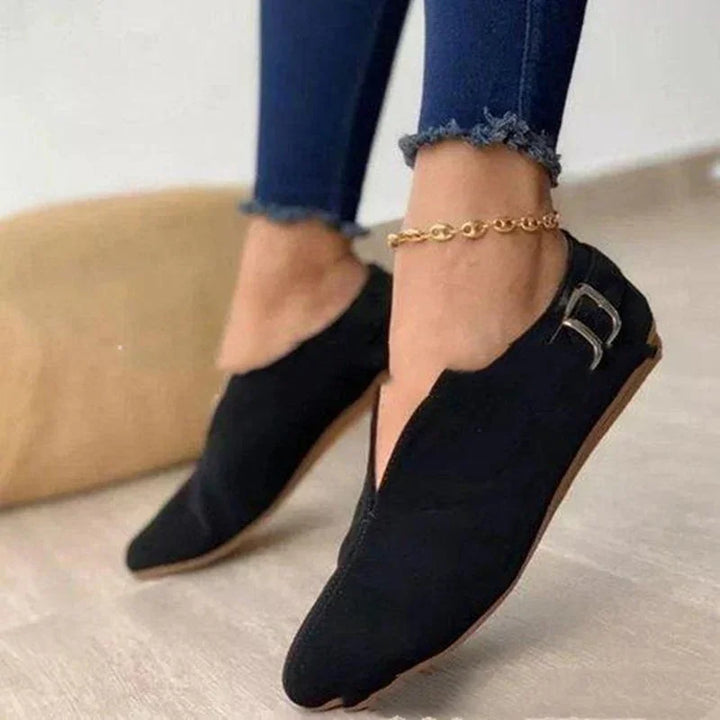 Woman wearing black pointed flat shoes with side buckle and gold anklet, paired with frayed hem jeans