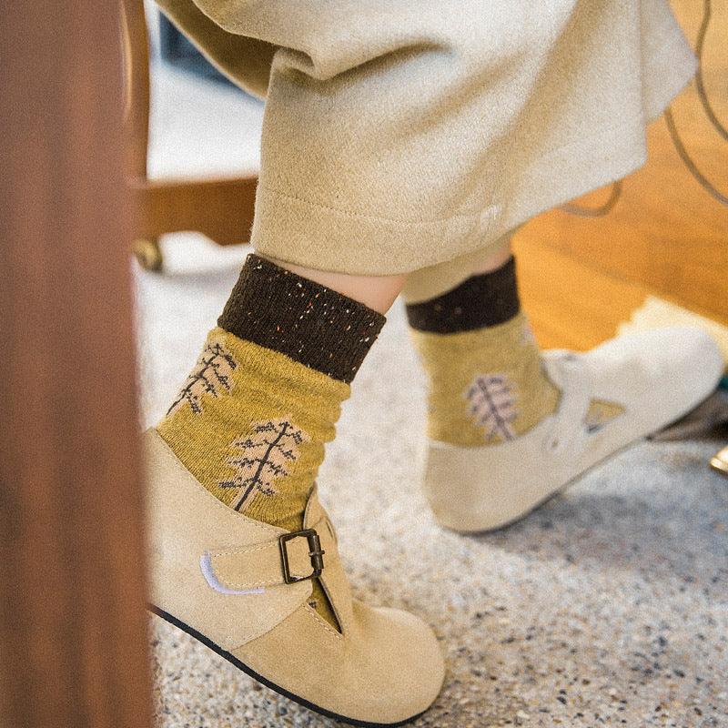 Beige buckle shoes worn with mustard yellow socks featuring tree patterns, paired with light beige pants indoors