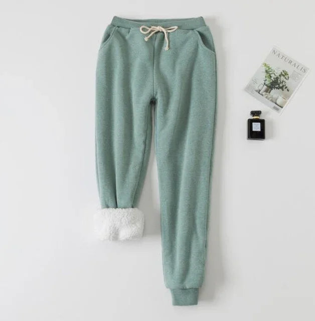 Green fleece sweatpants with drawstring and white sherpa lining on cuff, styled with a magazine and perfume