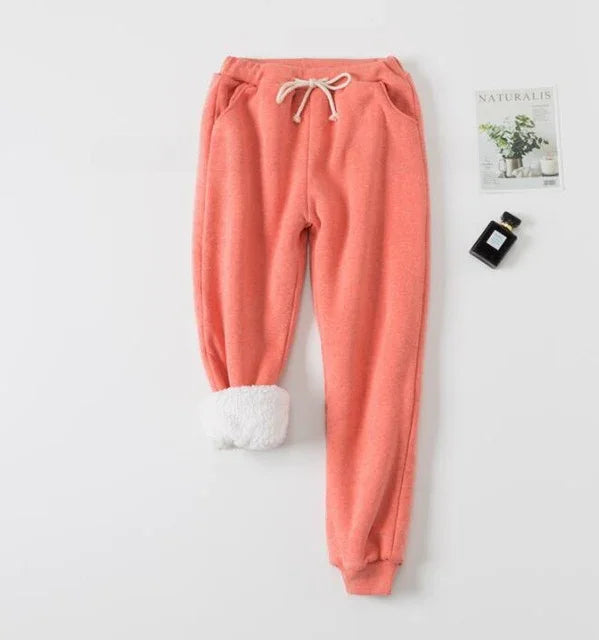 Coral pink fleece jogger pants with white drawstring and plush lining on one cuff, styled with perfume and plant magazine