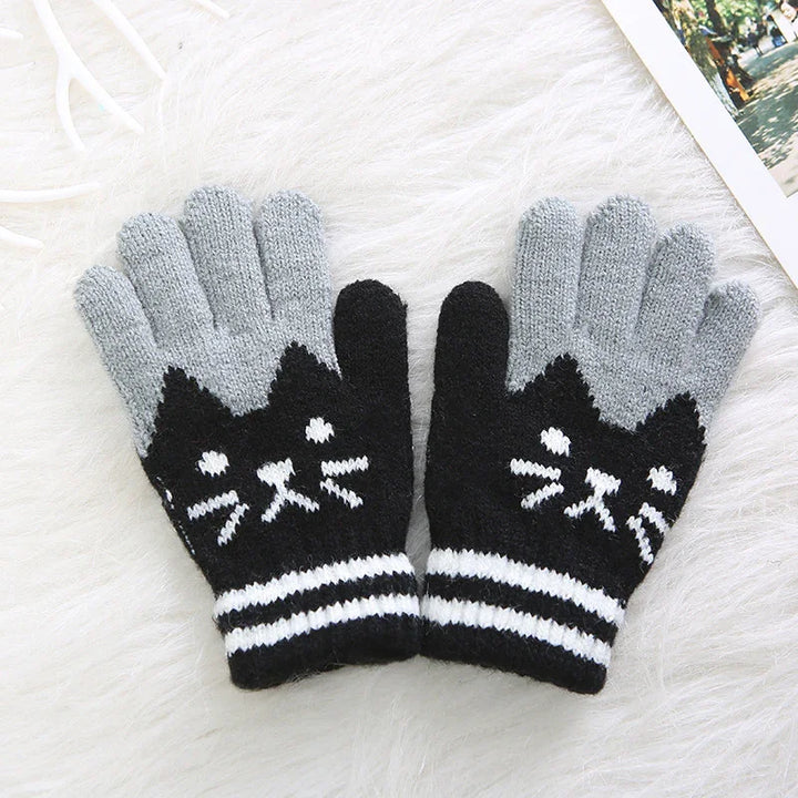 Pair of knitted gloves with black cat face design and grey fingers on white faux fur background