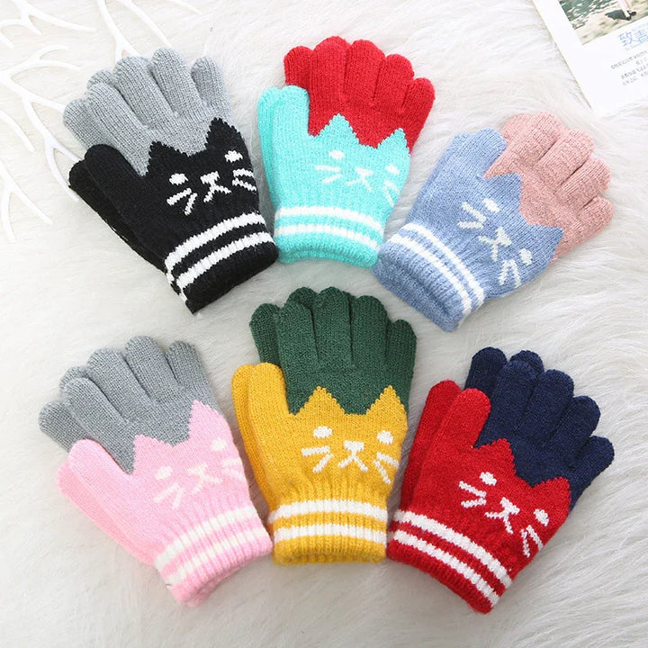 Colorful knitted gloves with cute cat face designs arranged on a white fluffy surface