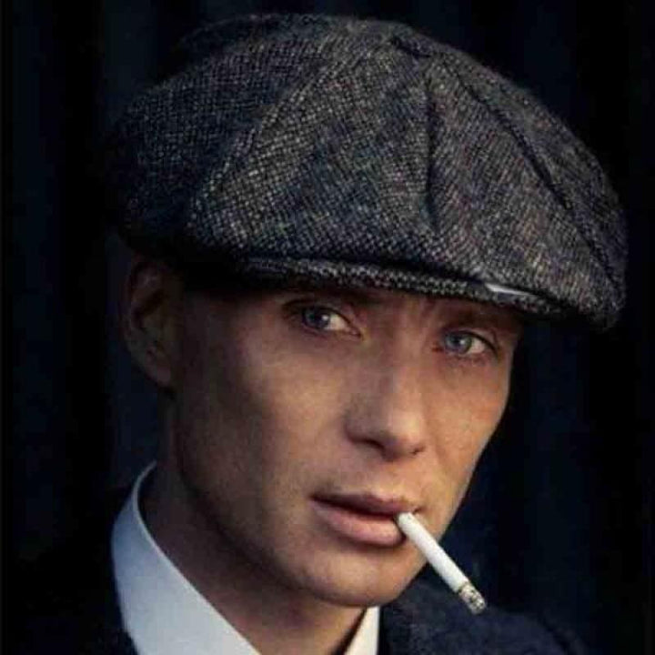 Close-up of man wearing grey tweed flat cap smoking cigarette with serious expression