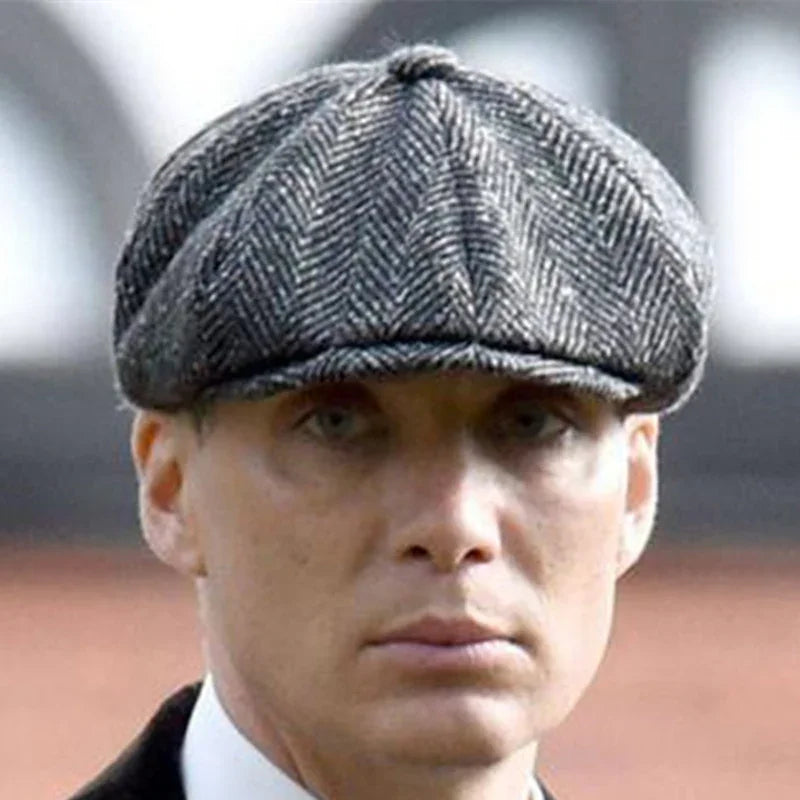 Close-up of a man wearing a gray herringbone flat cap and a white shirt with a black jacket