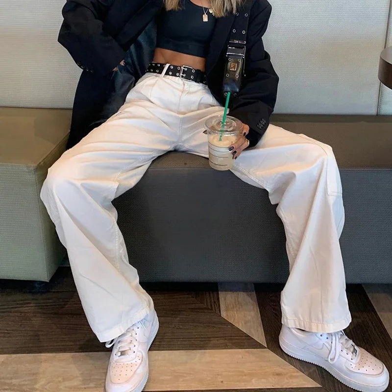 Person wearing white wide-leg pants, black crop top, black blazer, white sneakers, holding iced coffee