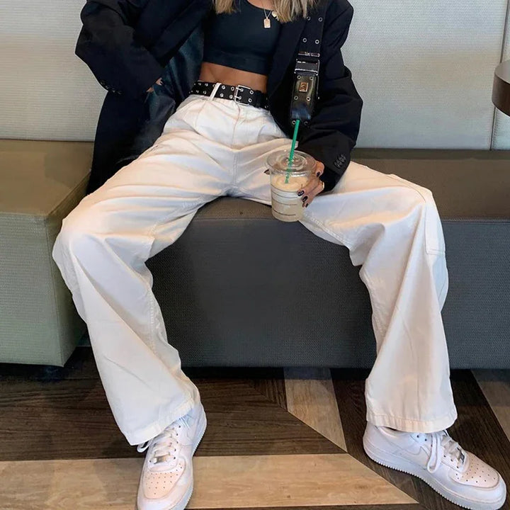 Person wearing white wide-leg pants, black crop top, black blazer, white sneakers, holding iced coffee