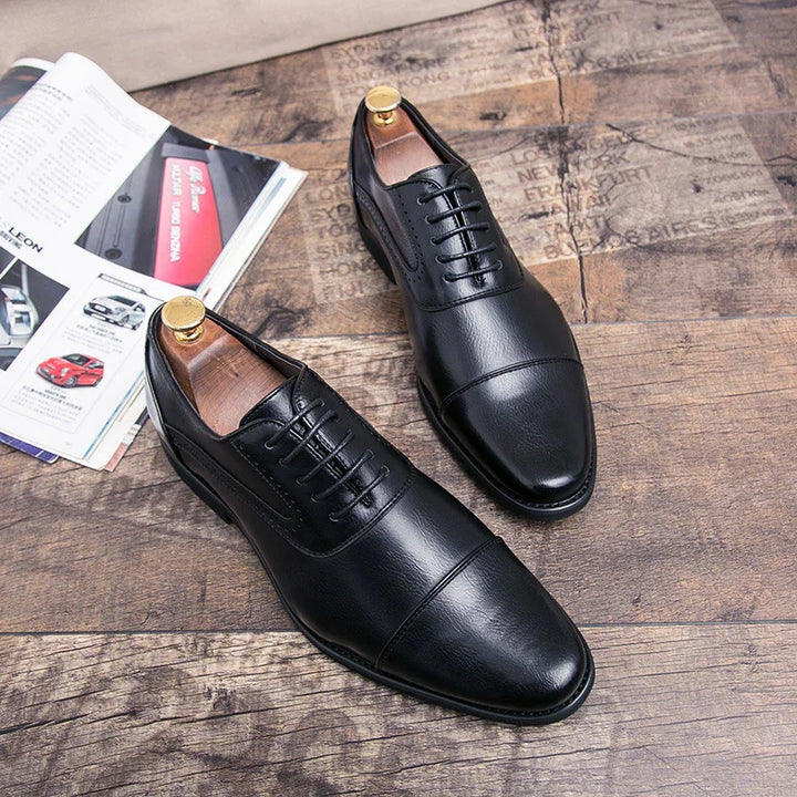 Pair of black leather dress shoes with laces on wooden floor beside open magazine