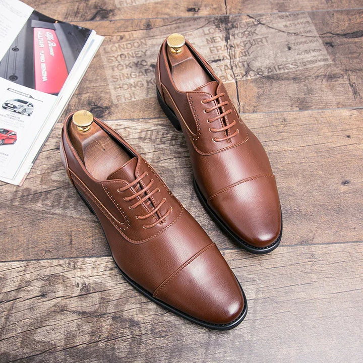 Pair of brown leather men's dress shoes with laces on wooden floor next to car magazine