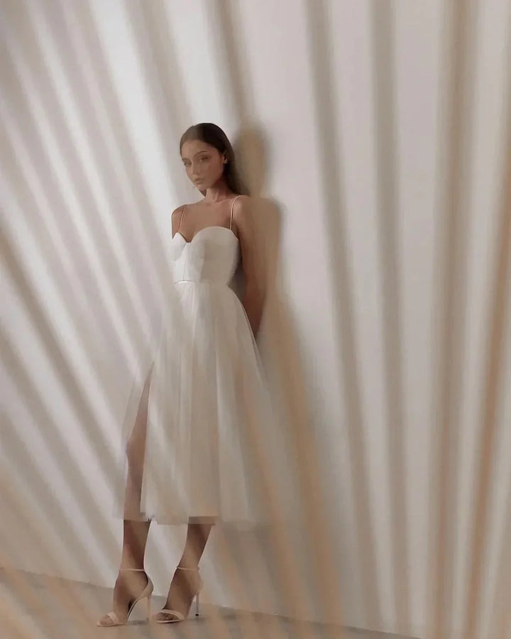 Woman in elegant white midi dress with slit and high heels against striped shadow background