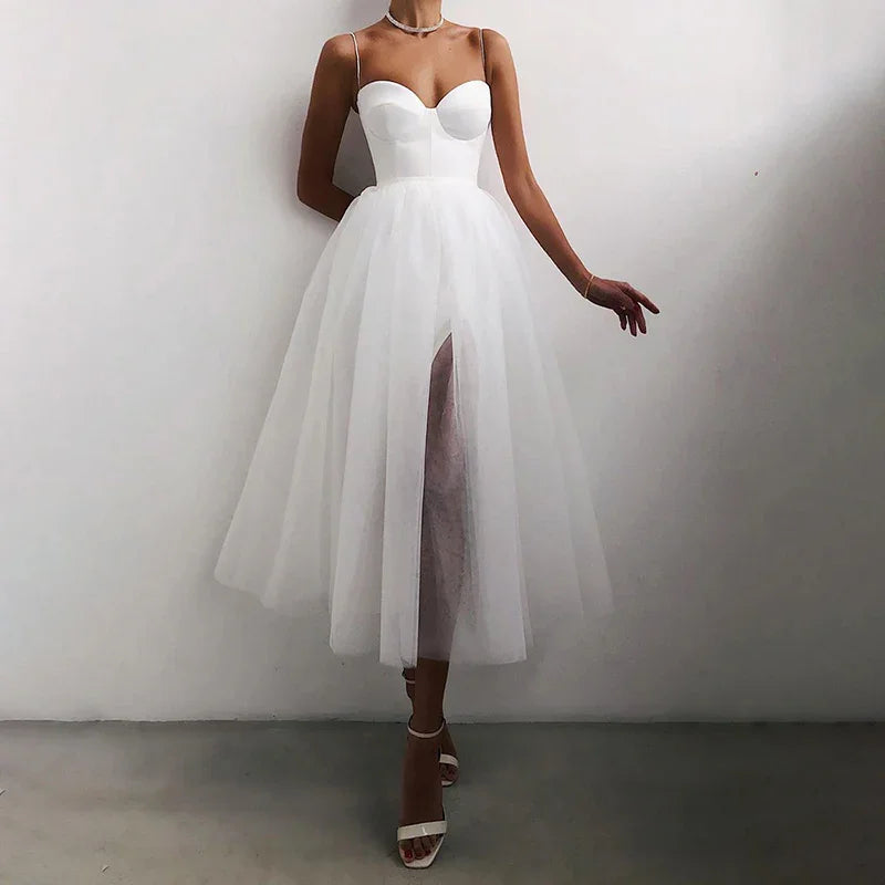 Woman wearing elegant white tulle midi dress with sweetheart neckline and slit, posing indoors