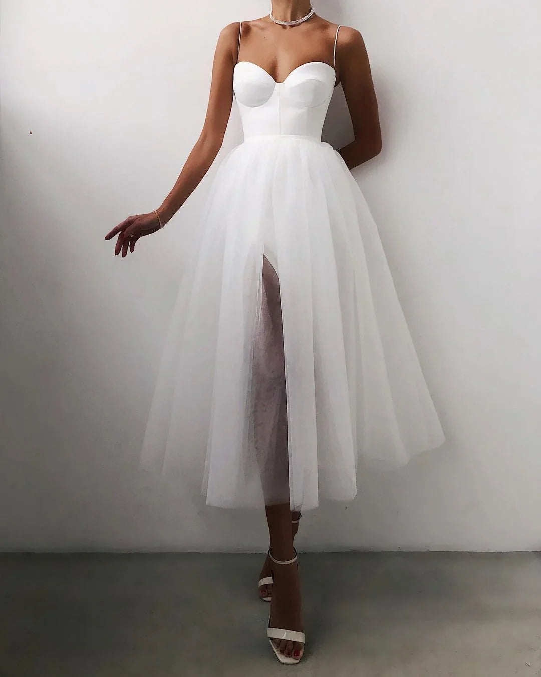 Woman in white midi dress with bustier top and tulle skirt with front slit, wearing white heels