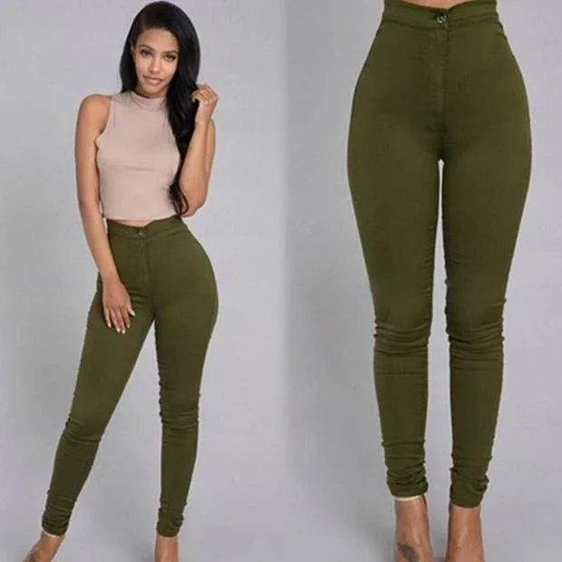 Woman wearing high-waisted olive green skinny pants and beige sleeveless crop top against gray background