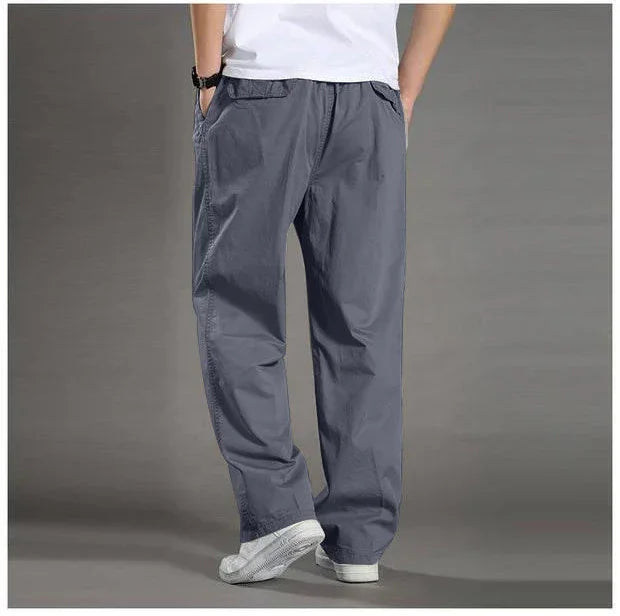 Man wearing loose fit gray casual pants and white sneakers on gray background