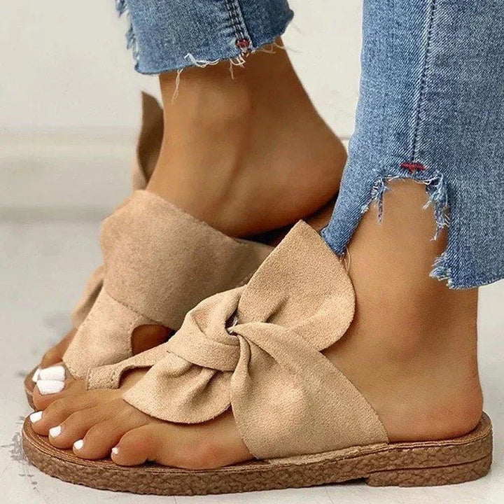 Close-up of feet in beige bow slide sandals paired with distressed hem skinny jeans