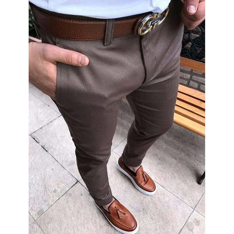 Man wearing brown textured slim-fit trousers with a brown belt and brown leather tassel loafers on tiled ground